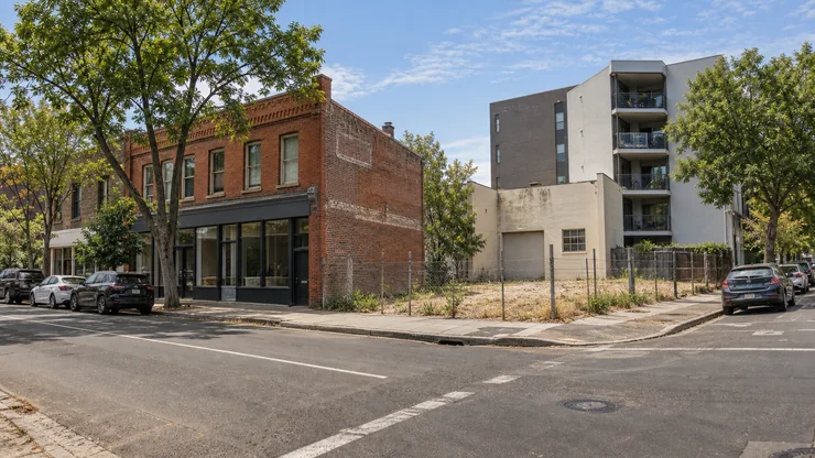 An urban street with contrasting building types and an undeveloped corner parcel.